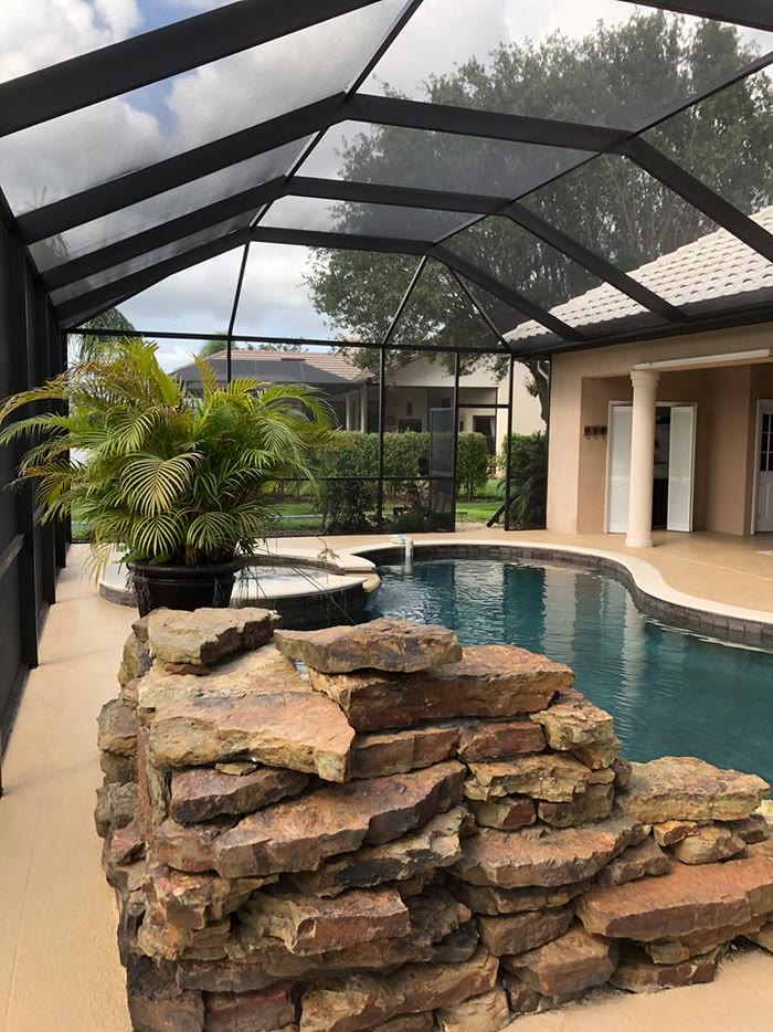 A rock waterfall beside the pool inside a screened enclosure, the house behind.