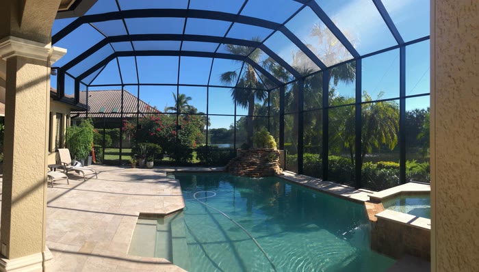 A clean screened enclosure over a pool with a rock waterfall and palms.