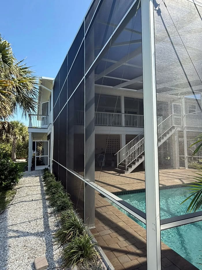 A two-storey screened enclosure beside a pool, its dark panels running the height of the house.