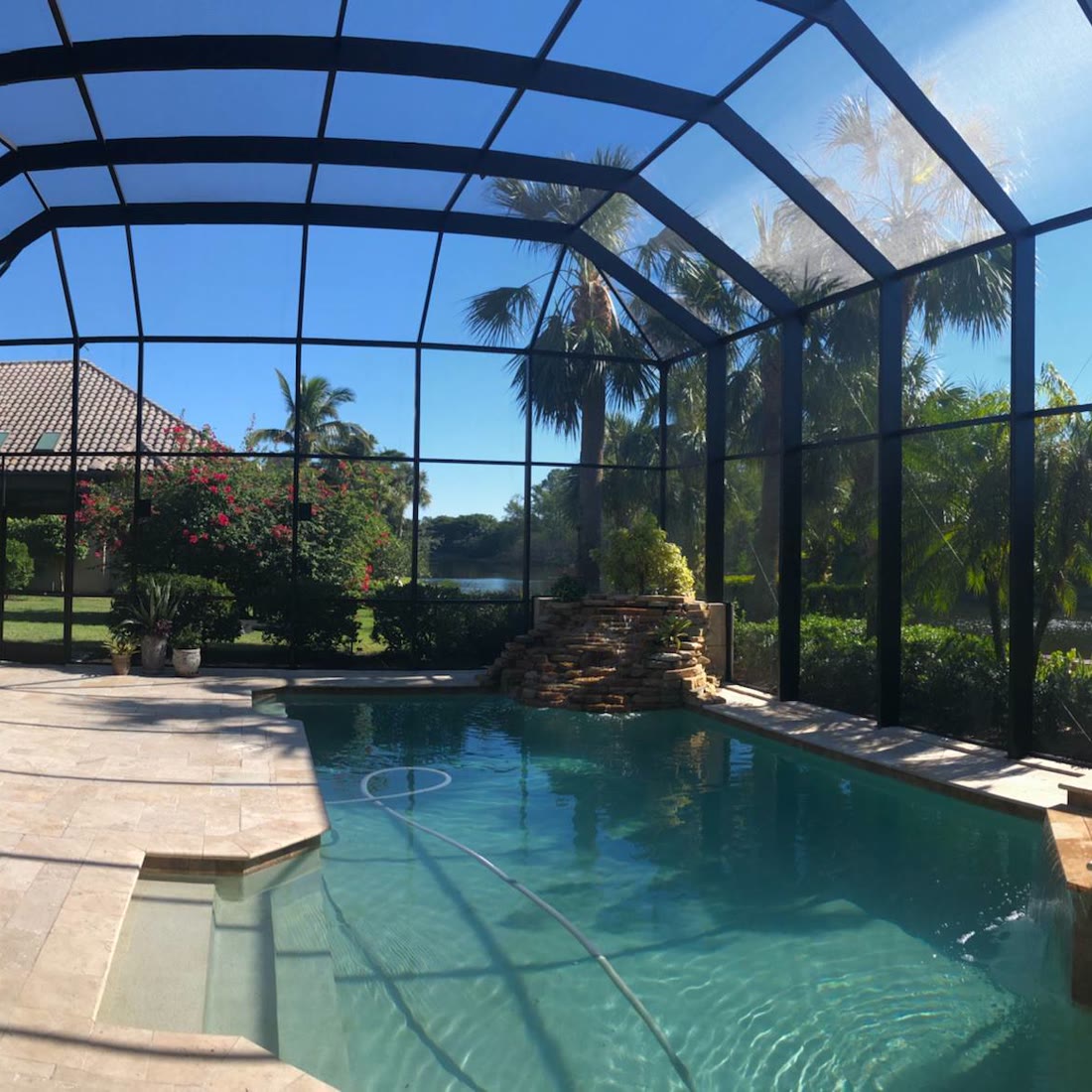 A clean screened enclosure over a pool with a rock waterfall and palms.