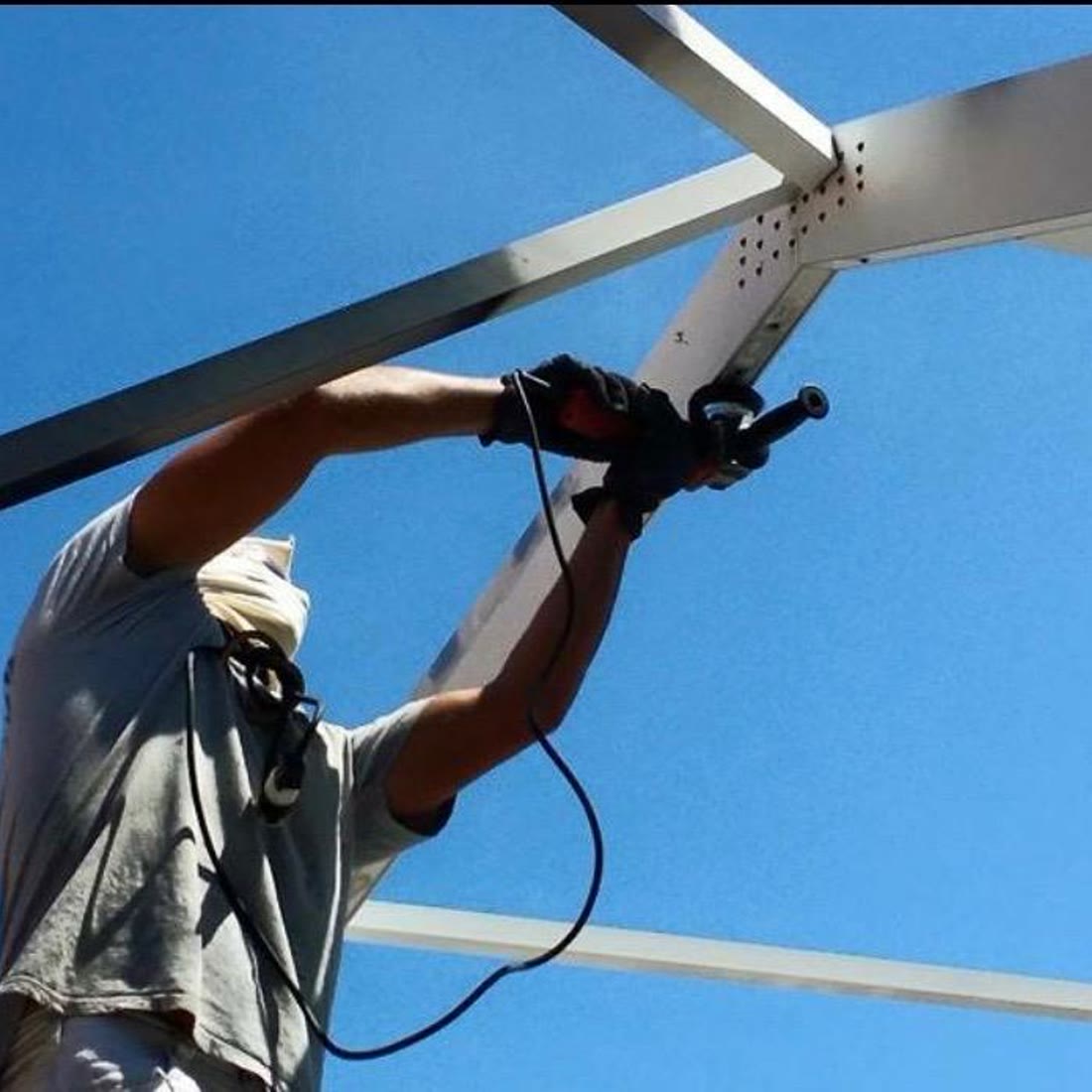 A painter reaching overhead, spray gun in both hands, working along a cage beam.